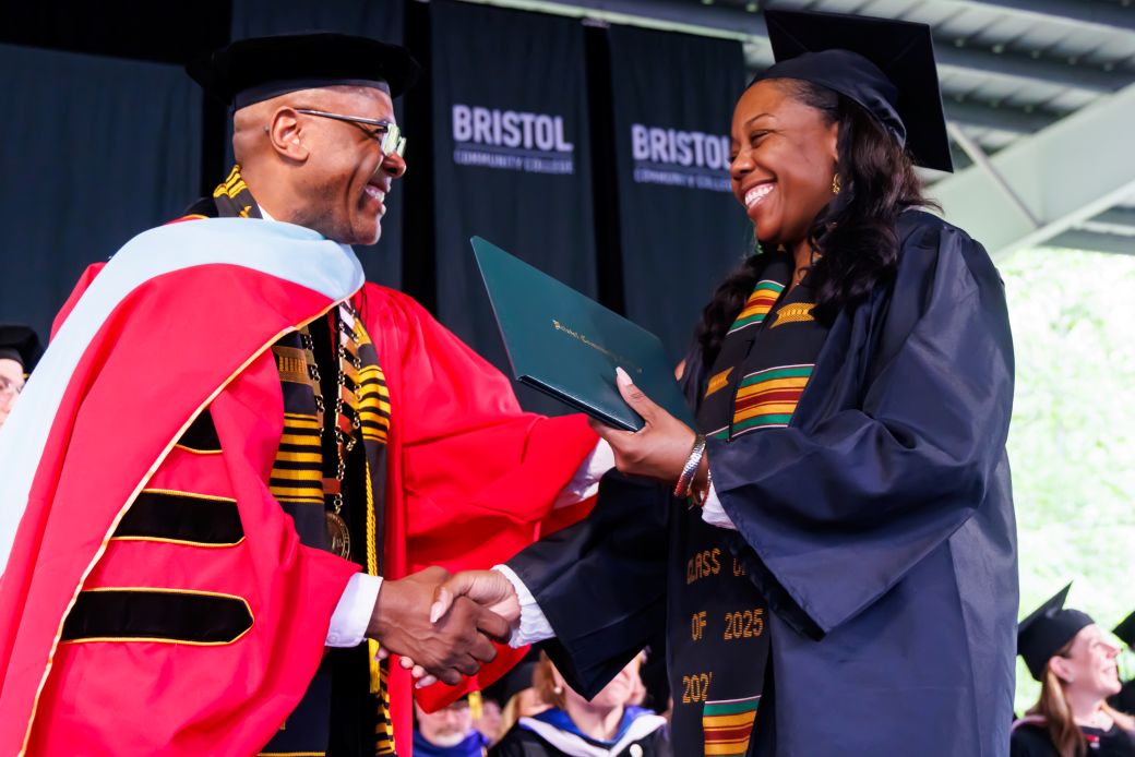 A graduation ceremony where a smiling graduate receives a diploma and shakes hands with a faculty member in regalia, conveying pride and achievement.