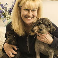 person with blonde hair smiling and holding two brown dogs